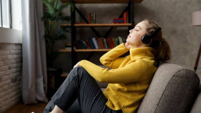 Beautiful pleased woman listening to music in headphones while sitting on sofa at home. High quality photo